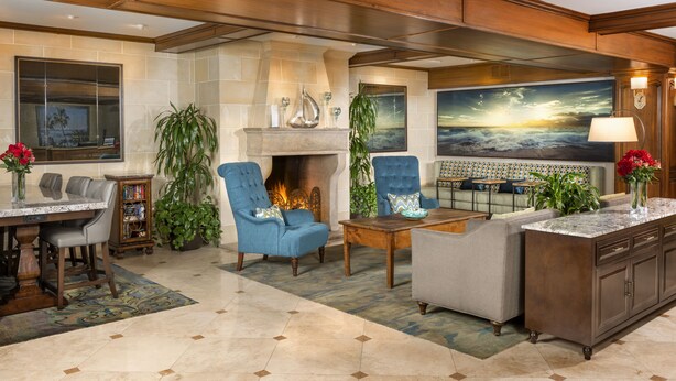 A spacious living area with a fireplace, comfortable seating, and a large painting of a sunset. - Ayres Hotel Laguna Woods - Aliso Viejo (Laguna Woods)
