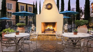 An outdoor patio with a stone fireplace, metal chairs, and potted plants. - Ayres Hotel Laguna Woods - Aliso Viejo (Laguna Woods)