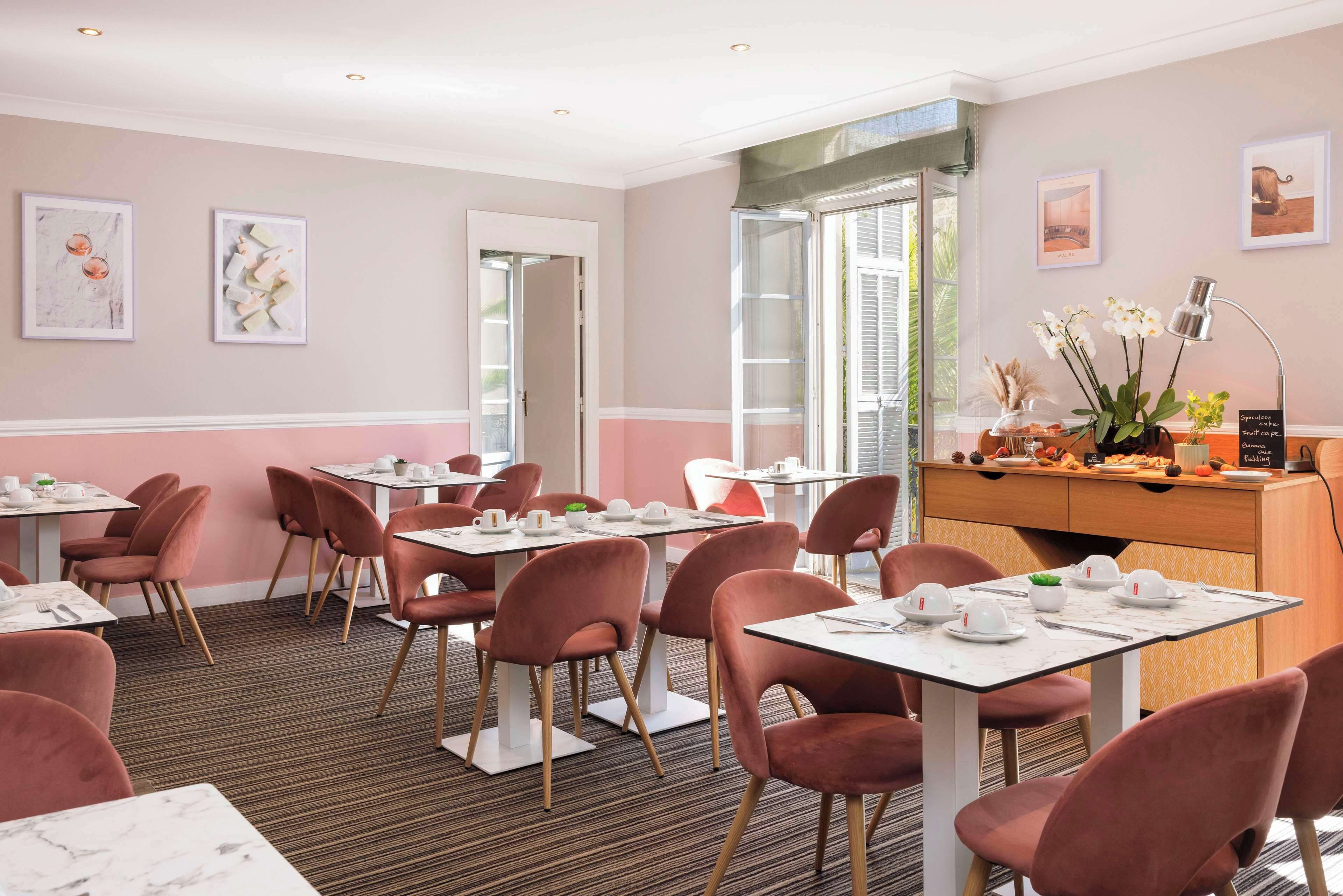 A dining area with tables and chairs, framed artwork on the walls, and a view of the outdoors.