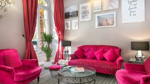 Una habitación con un sofá rojo, dos sillones rojos, una mesa de centro de vidrio y un ventanal con cortinas rojas.