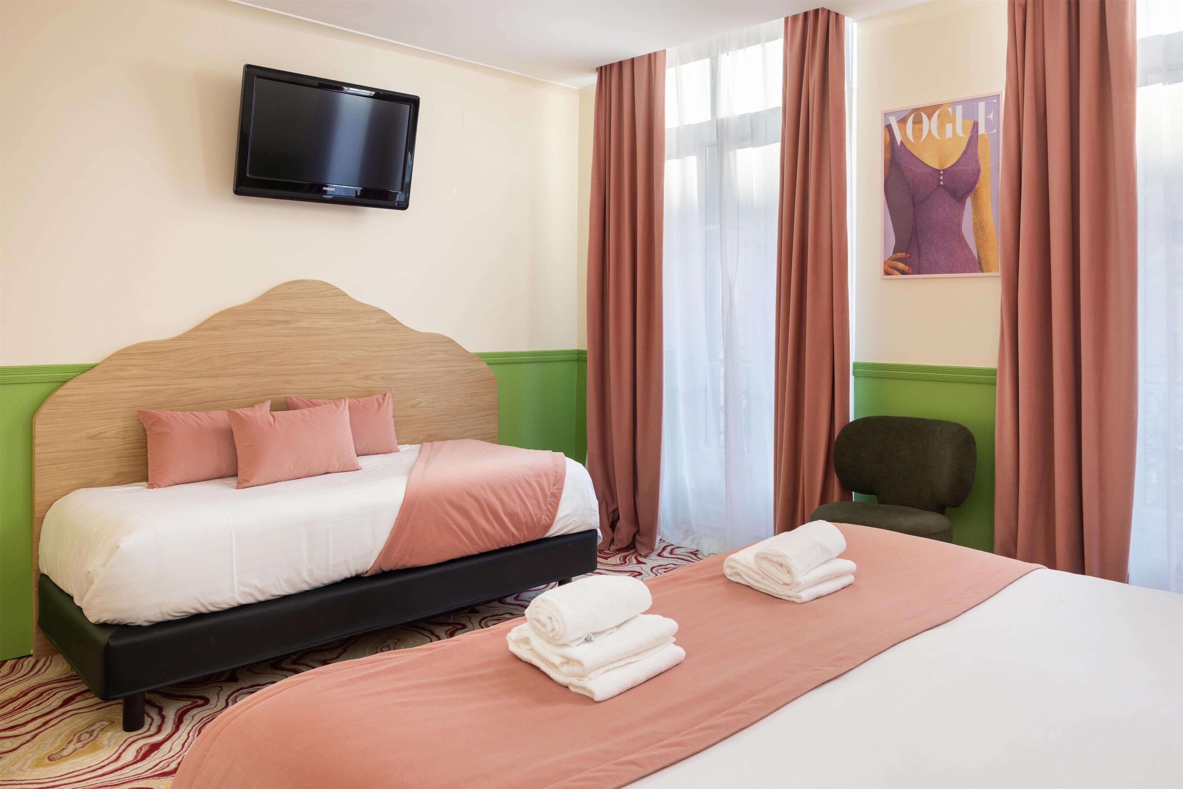 Een hotelkamer met een bed, een aan de muur bevestigde televisie, een stoel en een raam met gordijnen.
