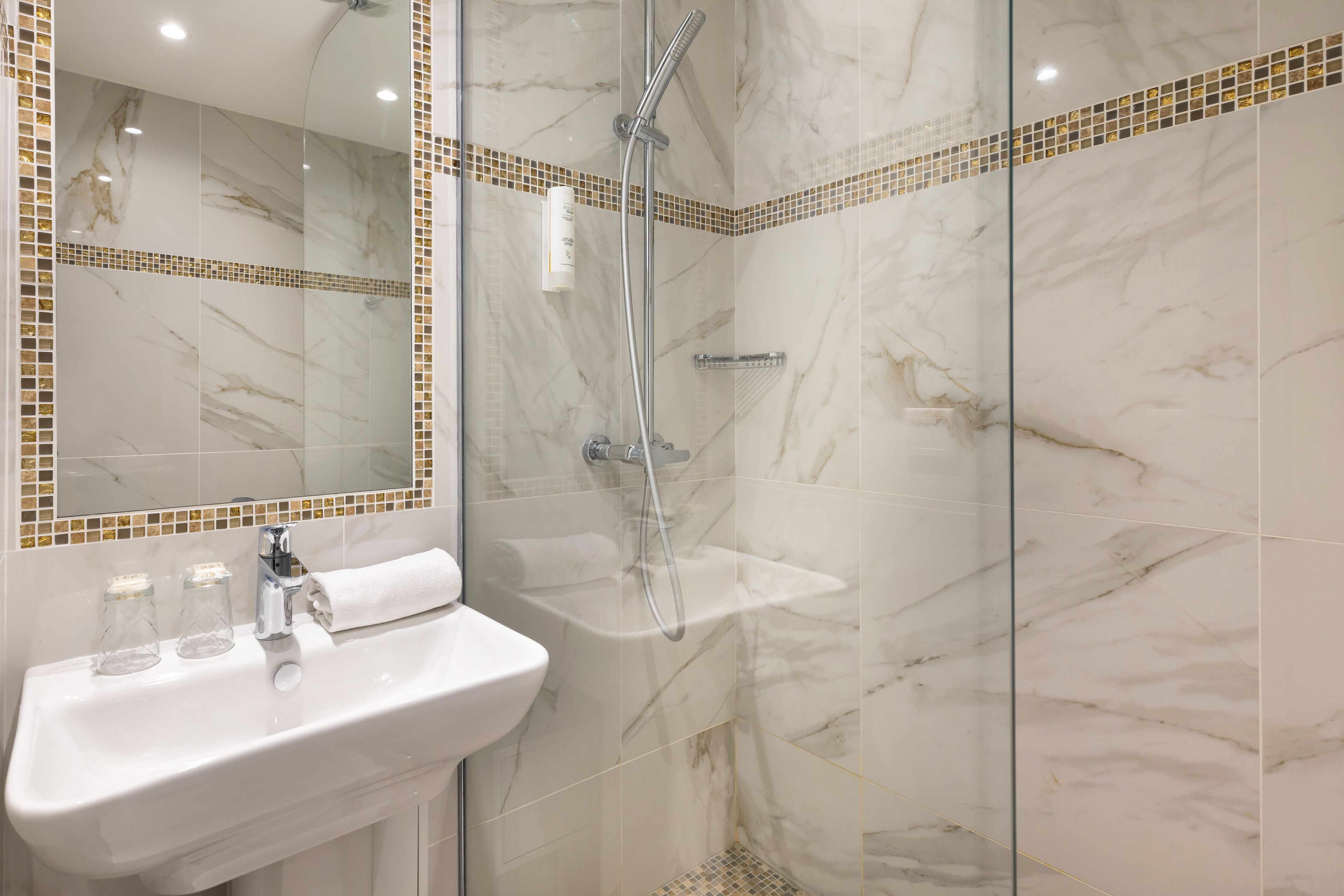 A bathroom with a white sink, a mirror, and a shower area with a glass door.
