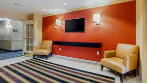 Een hotel lobby met een rode accentmuur, twee leren fauteuils, een flatscreen televisie en een gestreept tapijt.