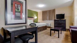Een hotelkamer met een bed, bureau, stoel, televisie, dressoir en een lijst aan de muur.