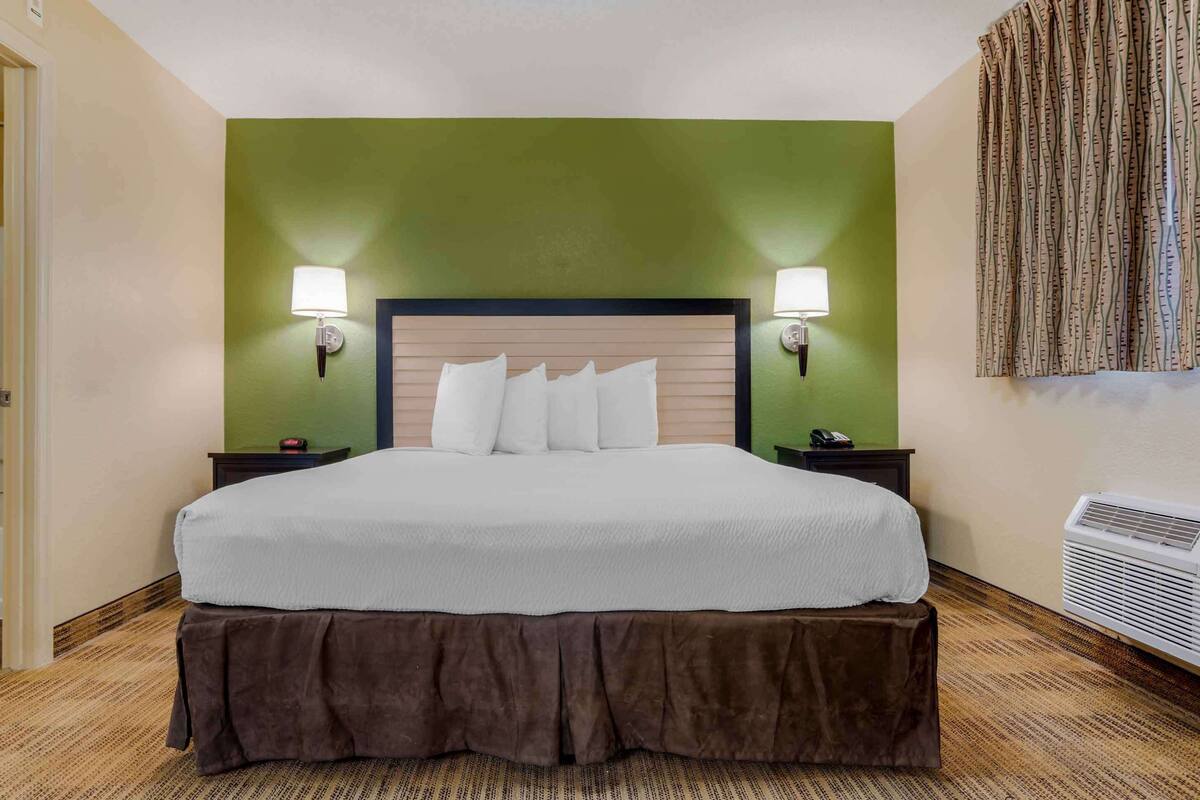 Ein ordentlich bezogenes Bett mit Holzkopfende, zwei Nachttischlampen und einem braunen Bettschurz.