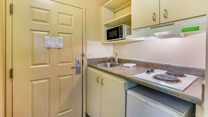 Een kleine kitchenette met een magnetron, fornuis, spoelbak en kastjes.