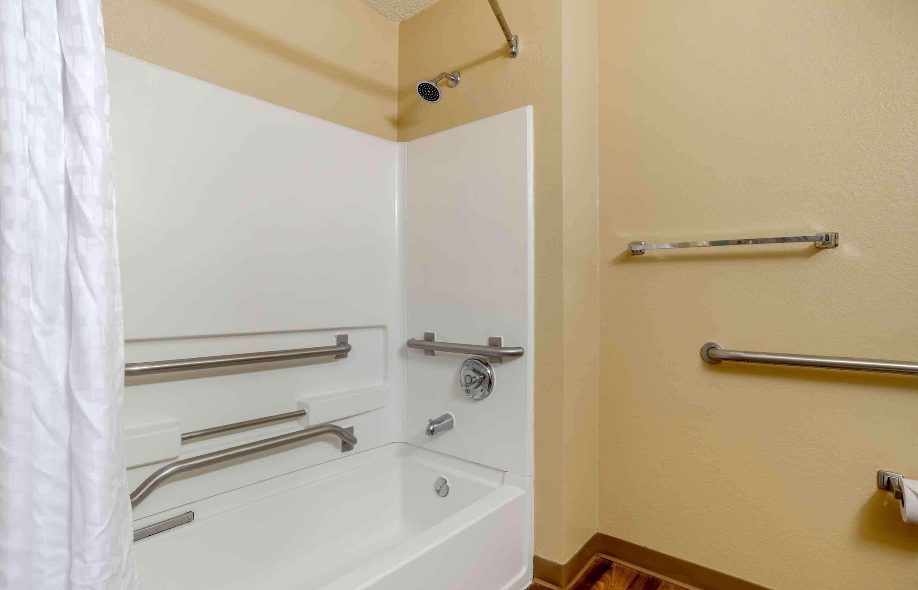 A bathroom with a bathtub, grab bars, and a showerhead.
