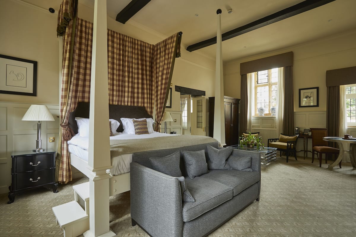 A bedroom with a four-poster bed, a grey sofa, a desk, and a chair.