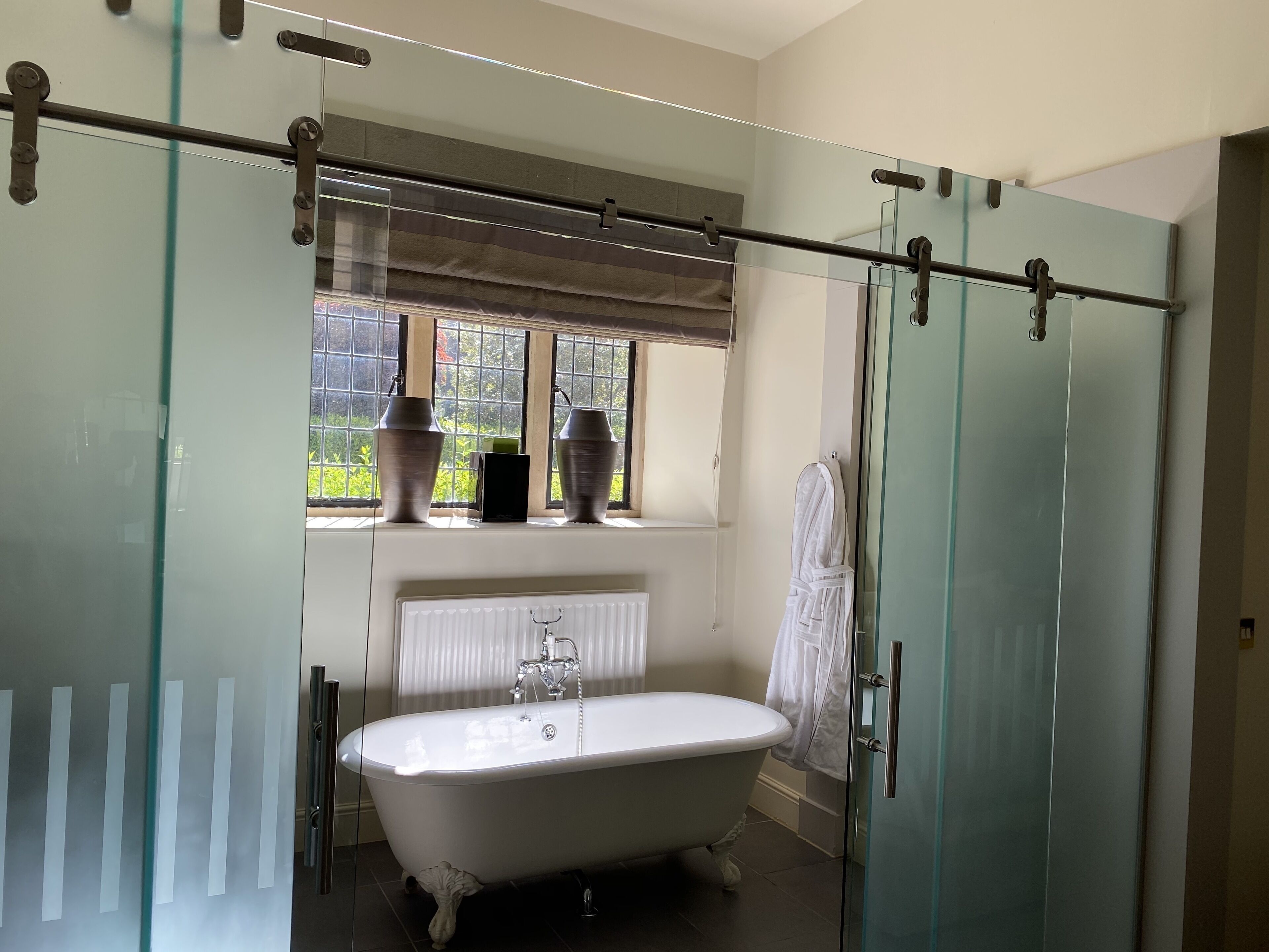 A bathroom with a freestanding bathtub, a window with a view of greenery, and a glass shower enclosure.