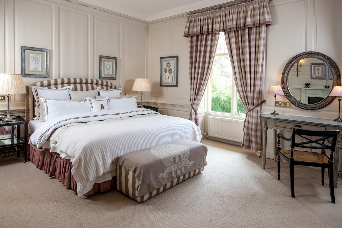 A bedroom with a large bed, bedside tables, a desk, a chair, and a window with curtains.