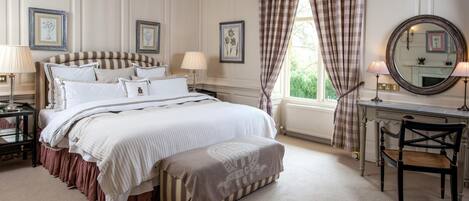A bedroom with a large bed, bedside tables, a desk, a chair, and a window with curtains.