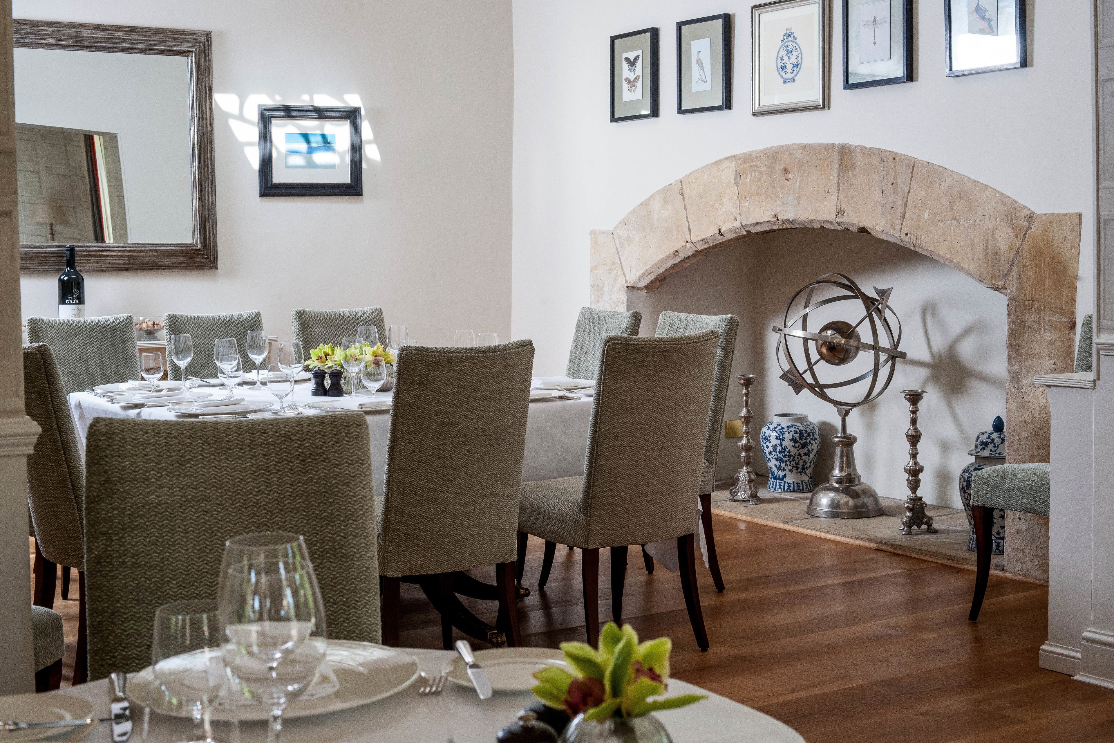 Uma sala de jantar com lareira, obras de arte emolduradas e uma mesa posta para refeição.