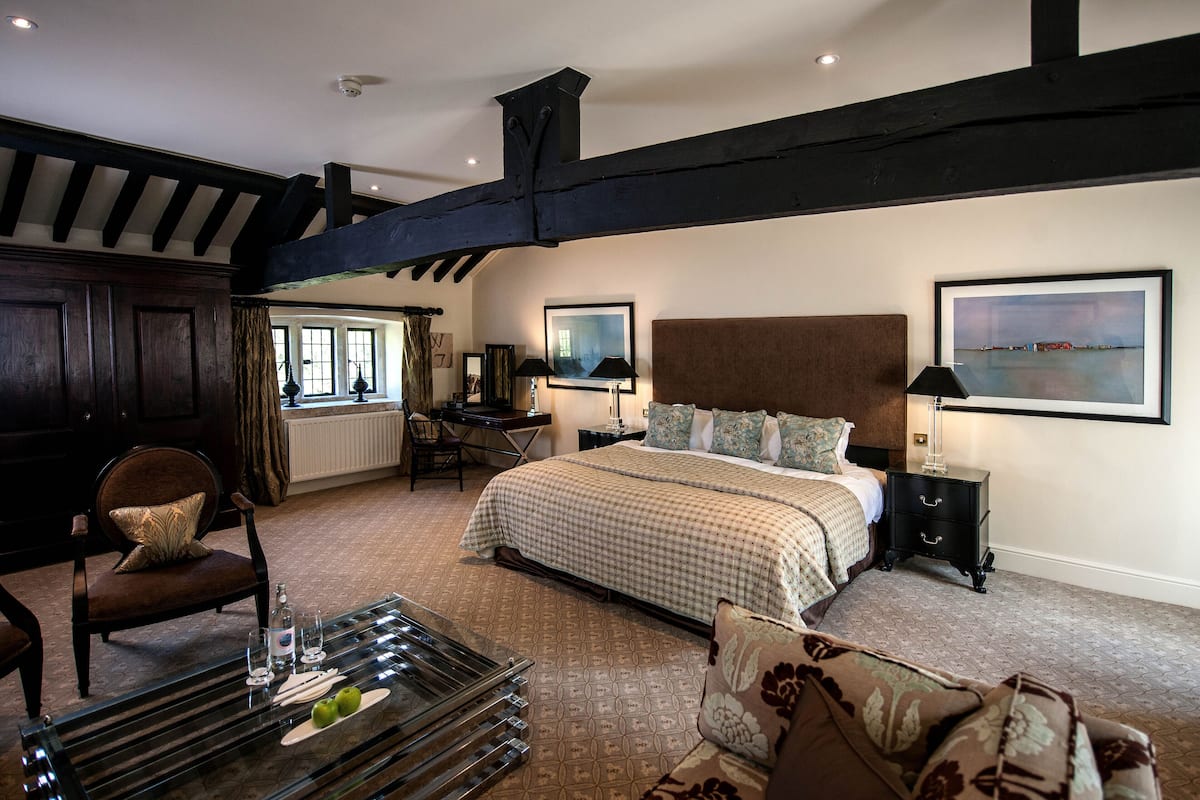 A bedroom with a large bed, a desk, and a chair. There is a window and a painting on the wall.