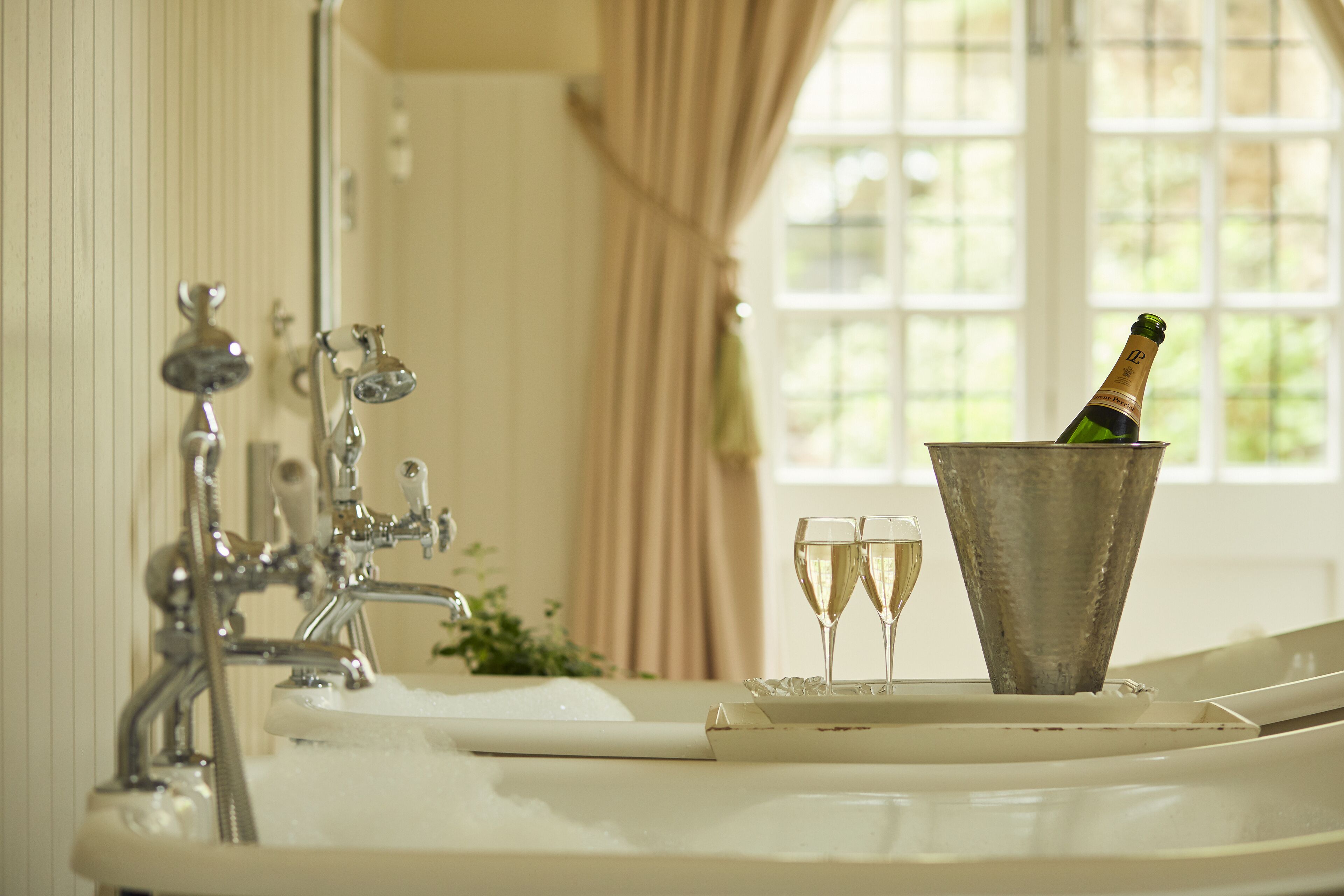 A bathroom with a bathtub, a champagne bottle in a bucket, and two champagne glasses.