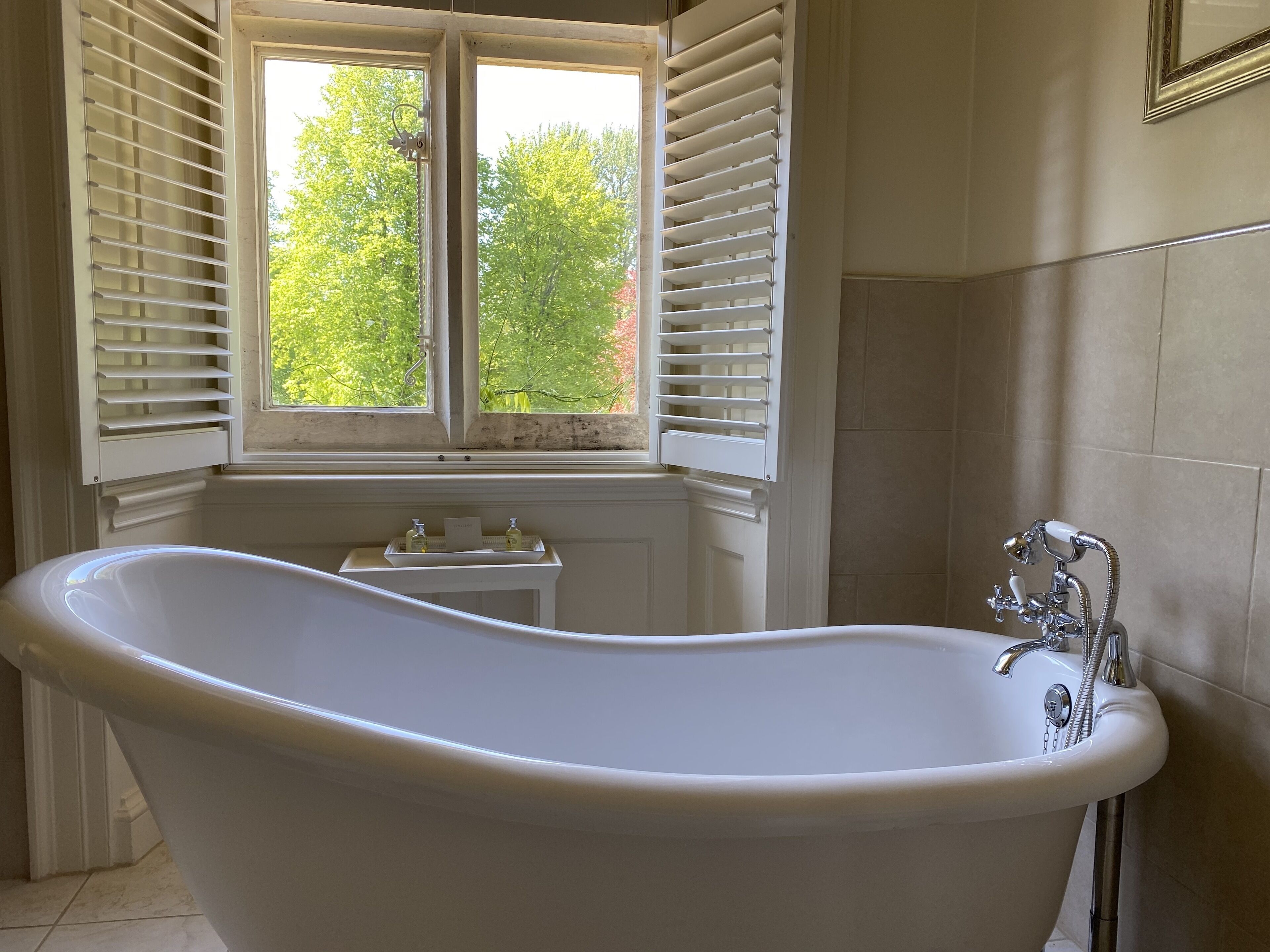 A bathroom with a freestanding bathtub, a window with shutters, and a sink with a faucet.