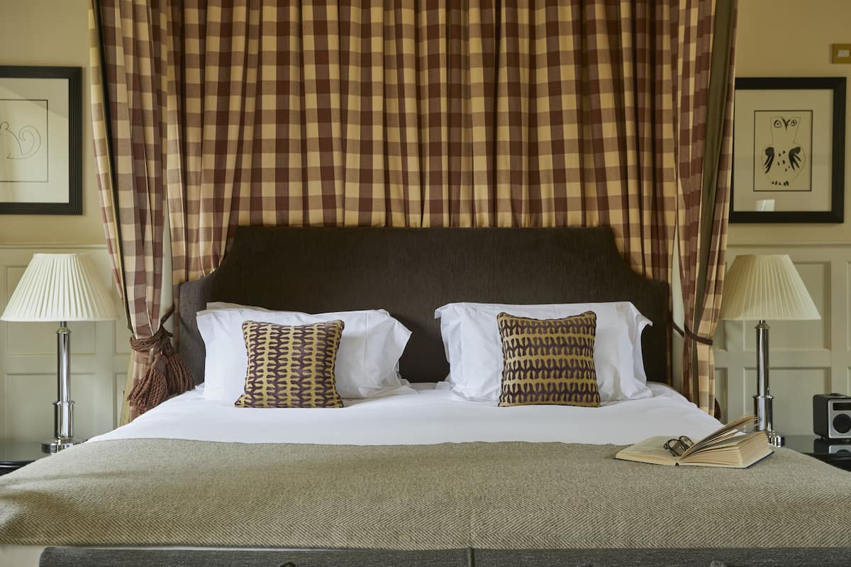 A neatly made bed with a checkered canopy, two bedside lamps, and a book on the bed.