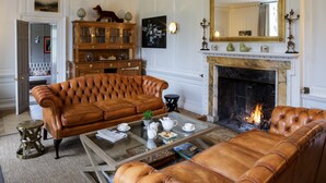 Una sala de estar con chimenea, sofás de cuero, una mesa de centro de vidrio y un aparador de madera.