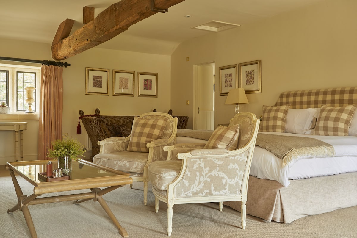 A room with a bed, two armchairs, a glass-top coffee table, and a fireplace.