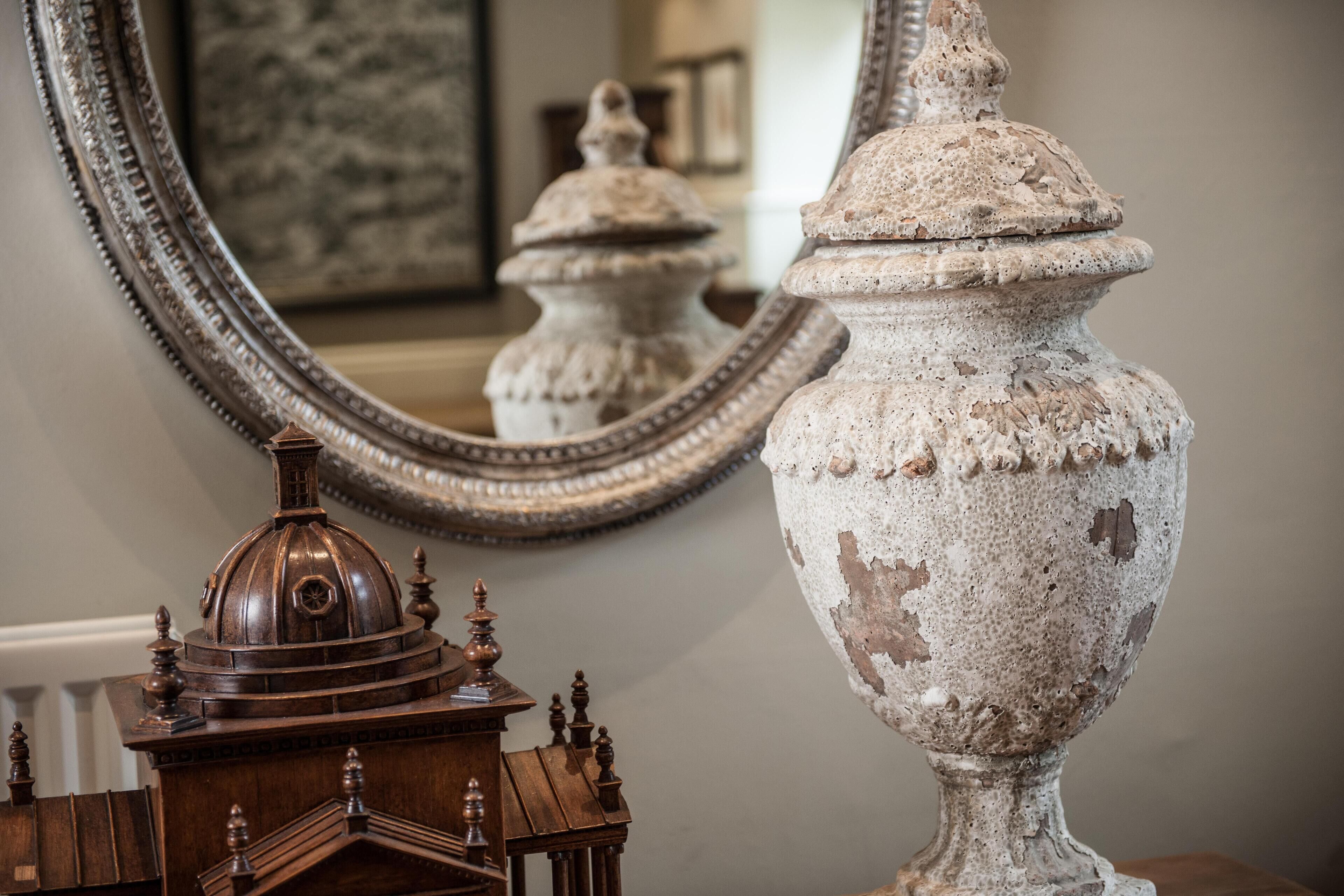 A large ornate mirror with a decorative frame, a rustic urn, and a wooden model of a building.