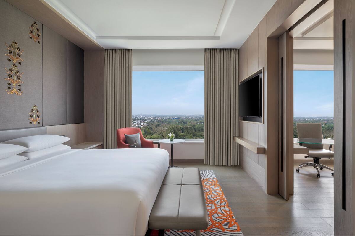 Una habitación de hotel moderna con una cama grande, zona de estar, televisor y vistas a la ciudad.