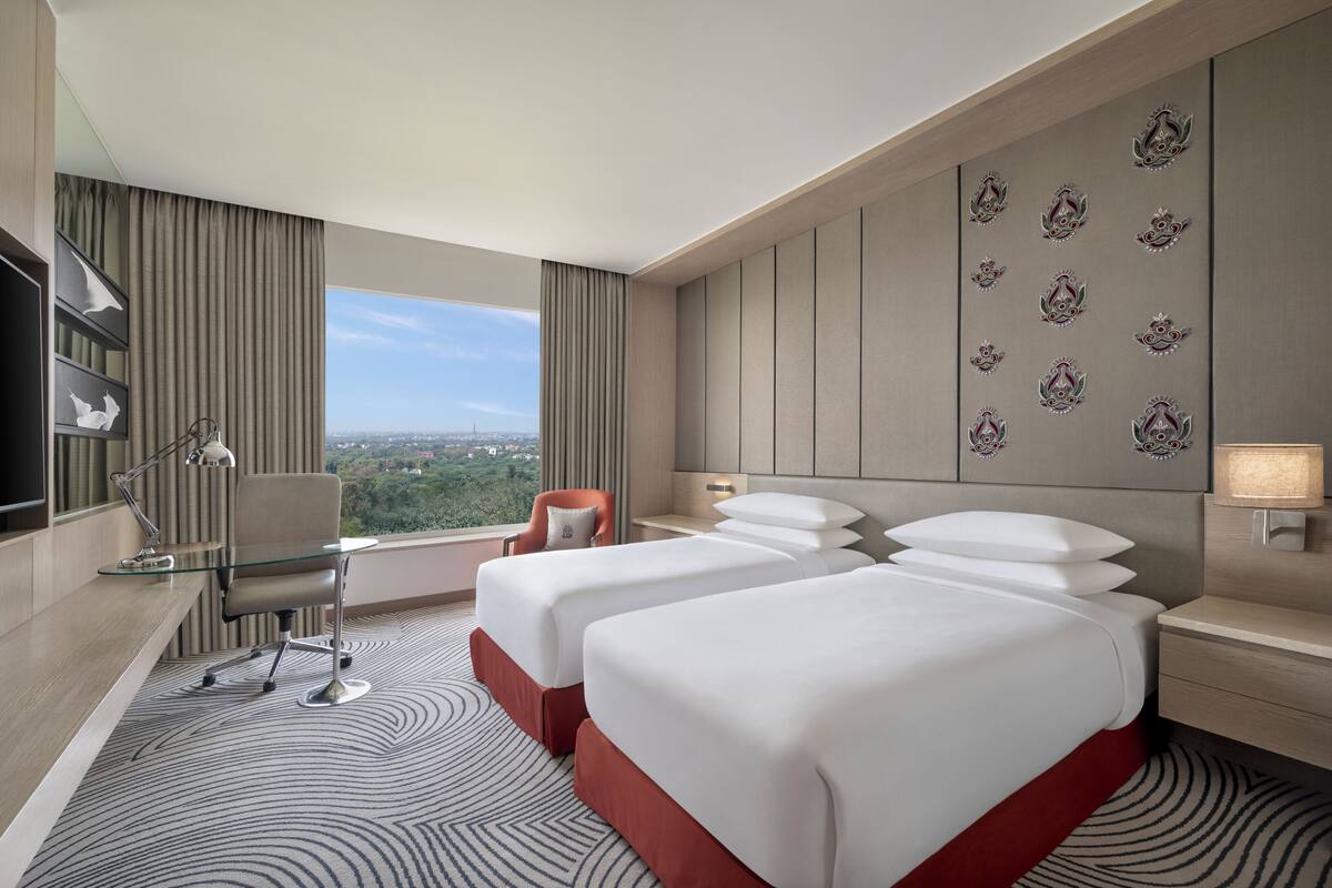 Habitación de hotel con dos camas, un escritorio, una silla, un televisor y vista a la ciudad.