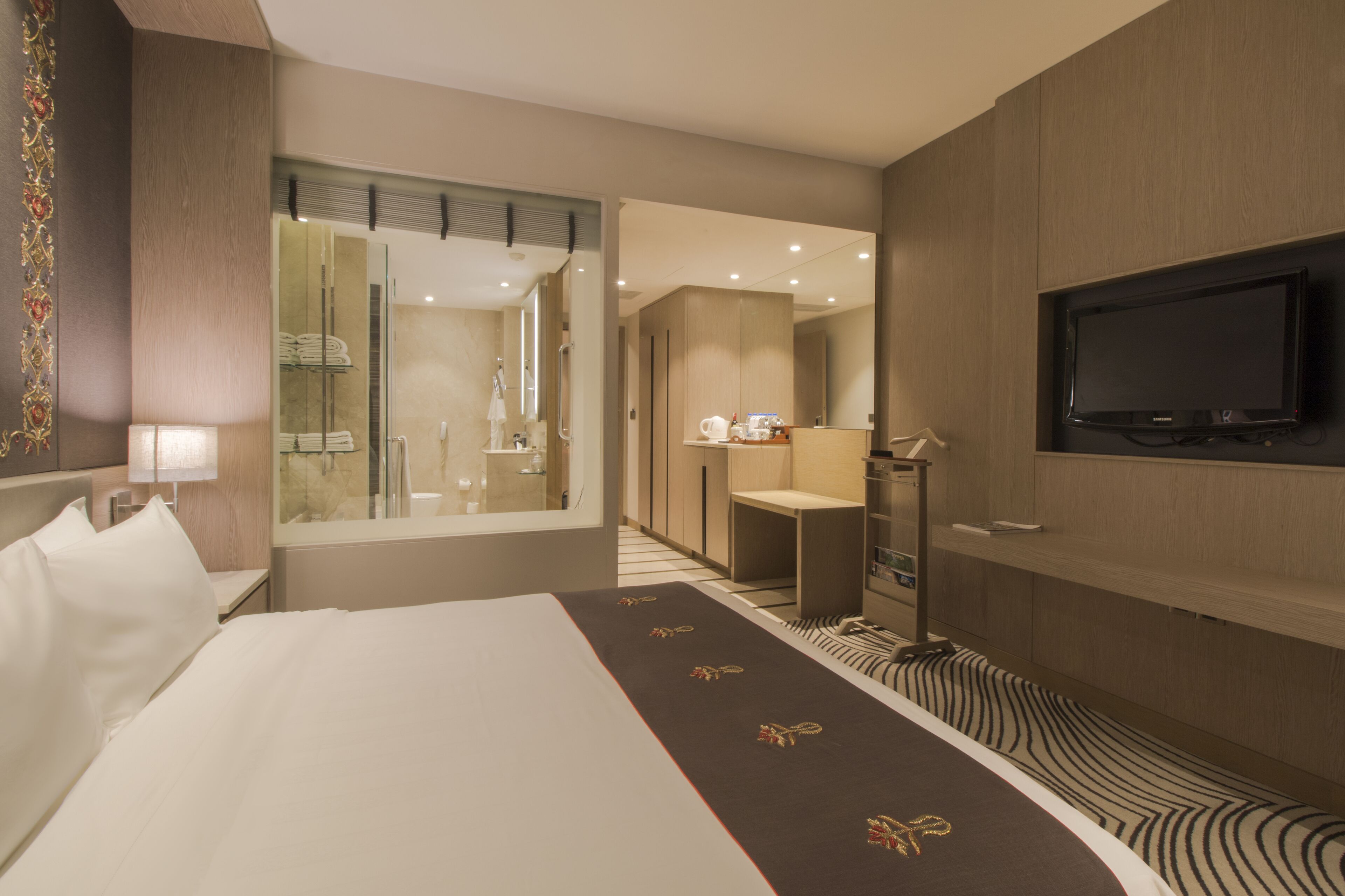 Una camera d'albergo con un letto grande, una TV fissata al muro, un bagno con specchio e porta asciugamani, e una piccola area relax.