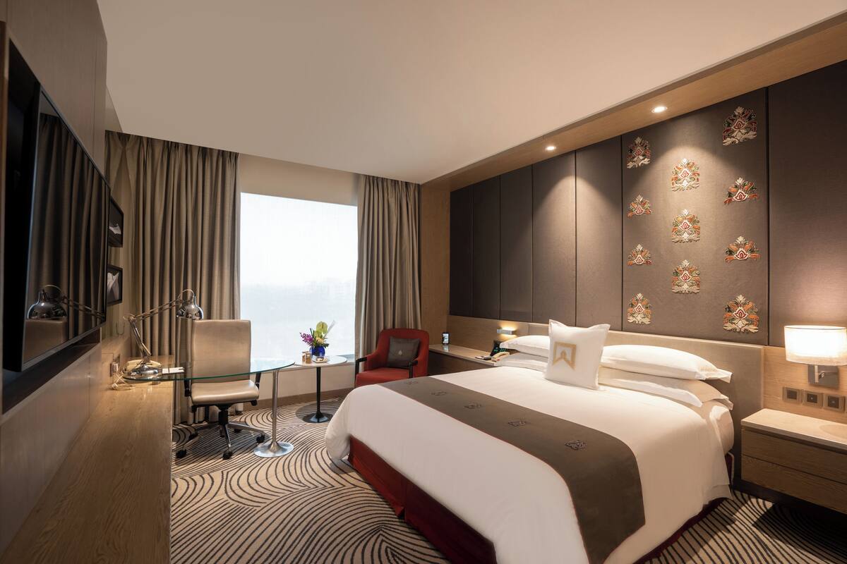 Habitación de hotel moderna con una cama grande, un escritorio, una silla y vistas a la ciudad.