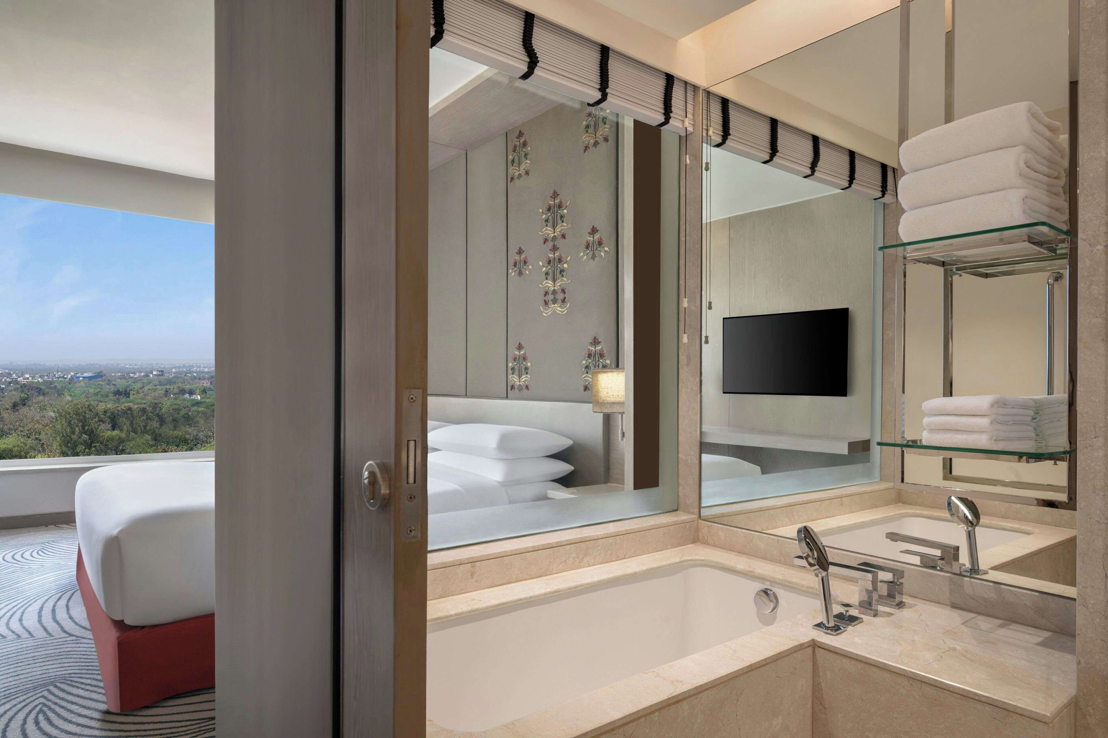 A modern bathroom with a large bathtub, a glass shelf with towels, and a large mirror.
