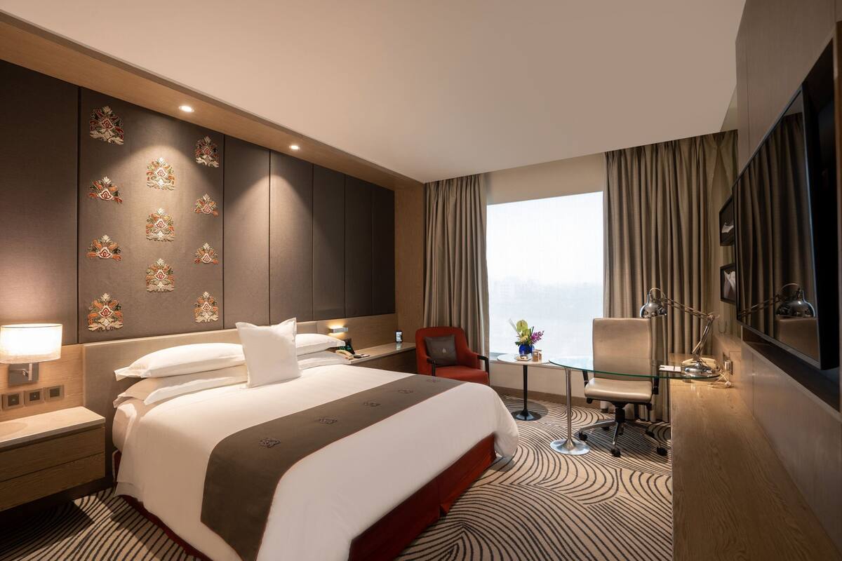 Una habitación de hotel moderna con una cama grande, un escritorio, una silla y vistas de la ciudad.
