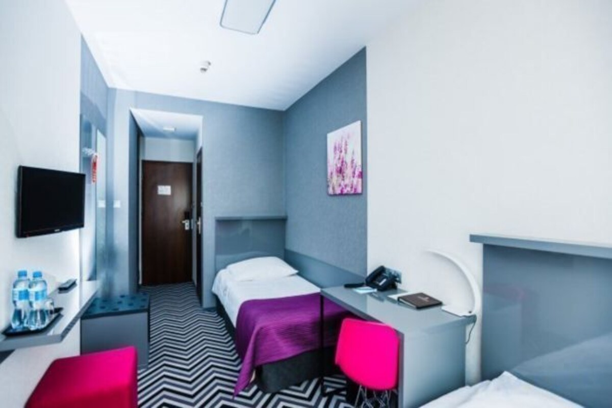 A hotel room with a bed, a desk, a chair, a TV, and a bathroom door.