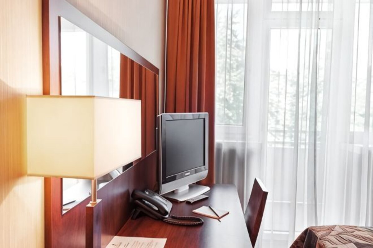 A hotel room with a desk, a television, a telephone, and a window with curtains.