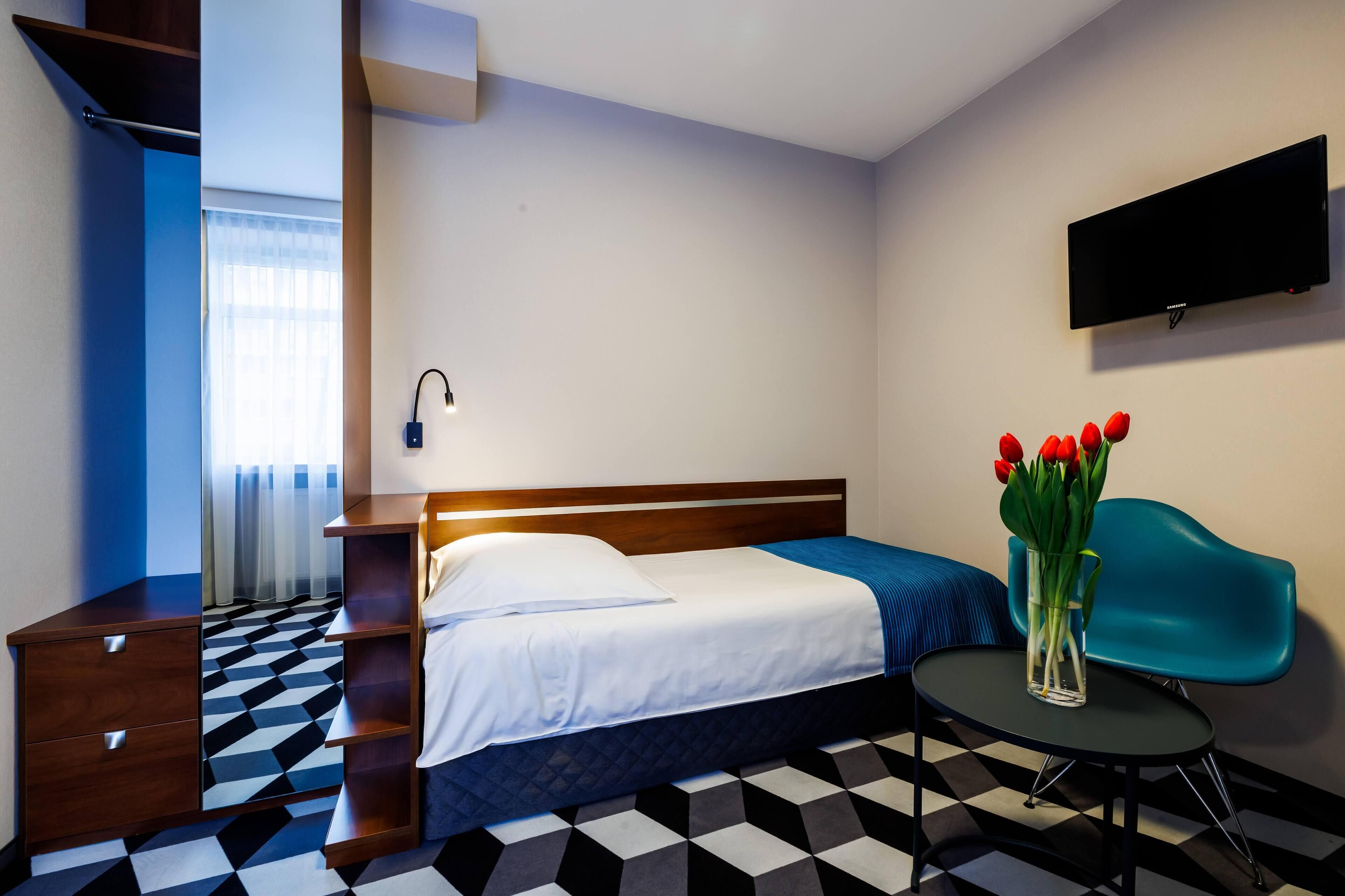 A hotel room with a bed, a desk, a chair, a TV, and a vase with flowers.