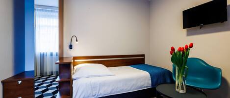 A hotel room with a bed, a desk, a chair, a TV, and a vase with flowers.