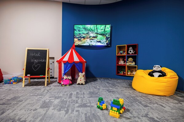 A children's play area with a tent, a television displaying a nature scene, and a shelf with stuffed toys. - Wyspianski Hotel (Kraków)