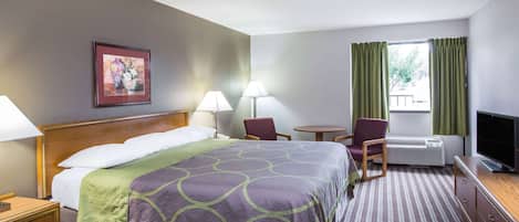 A hotel room with a bed, two chairs, a small table, a TV, and a window with curtains.