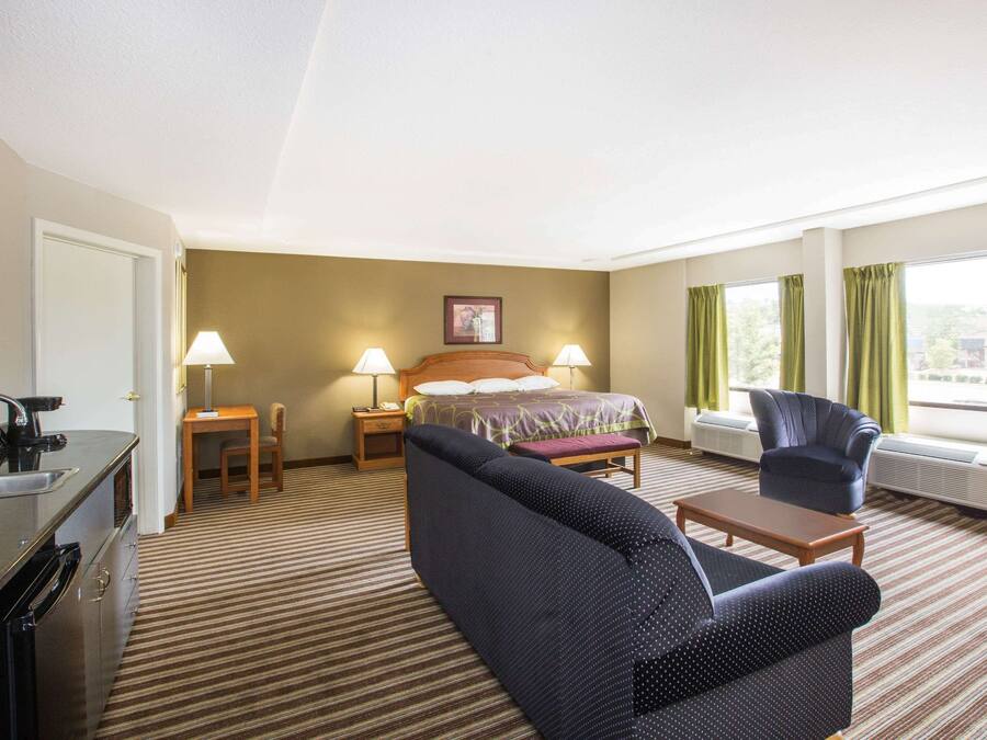 Habitación de hotel con cama, dos sillas, una mesita, un escritorio con lámpara y una ventana con cortinas.