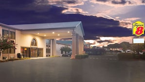 A Super 8 hotel with a covered entrance, a large parking lot, and a view of the sunset in the background.