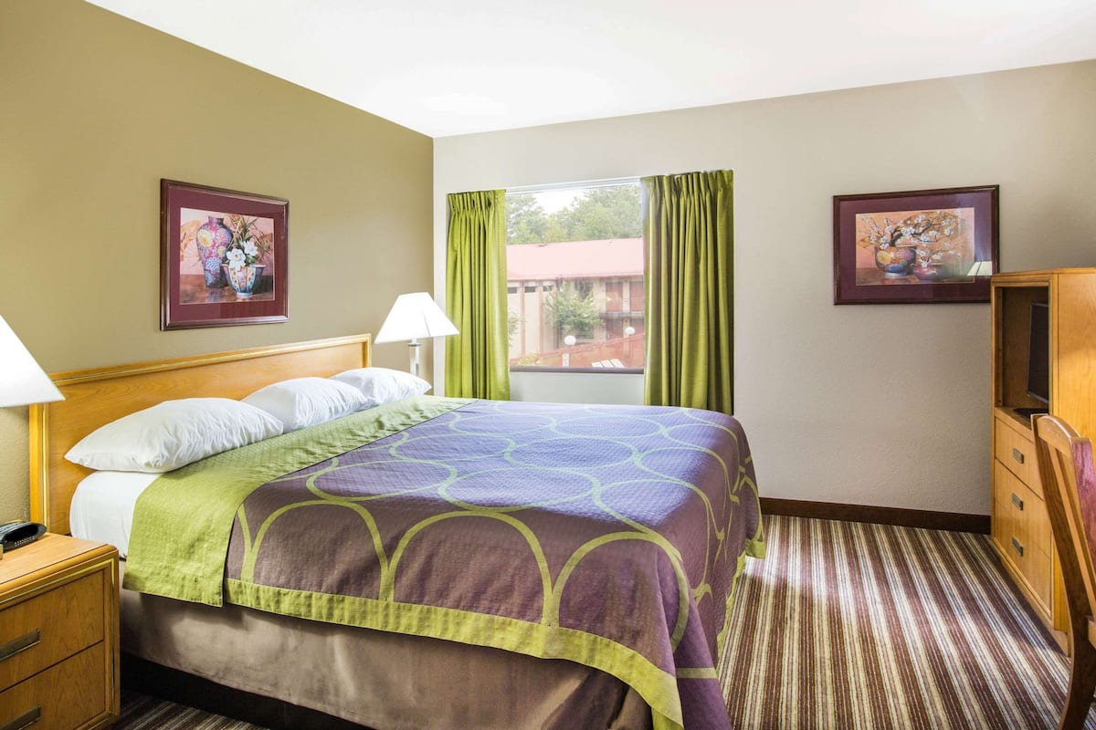 A hotel room with a bed, a nightstand, a lamp, a dresser, and two framed pictures on the walls.