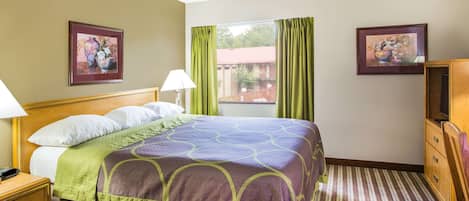 Une chambre d’hôtel avec un lit, une table de chevet, une lampe, une commode et deux tableaux encadrés accrochés aux murs.