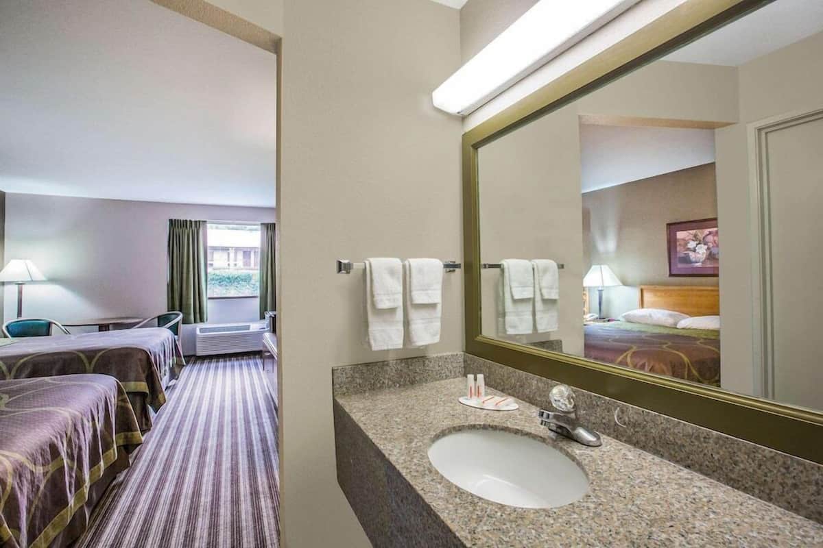 A hotel room with a bed, a bathroom with a sink and mirror, and a window with curtains.