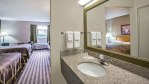 A hotel room with a bed, a bathroom with a sink and mirror, and a window with curtains.