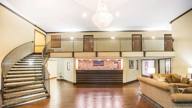A spacious lobby with a wooden staircase, a reception desk, and a seating area.
