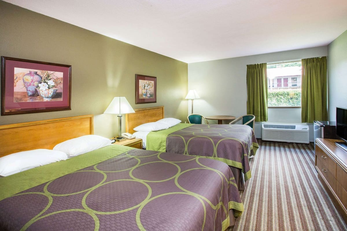 A hotel room with two beds, a desk, a chair, a TV, and a window with curtains.