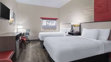 Ein Hotelzimmer mit zwei Betten, einem Schreibtisch, einem Sessel, einem Fernseher und einem Fenster mit Blick auf Bäume.