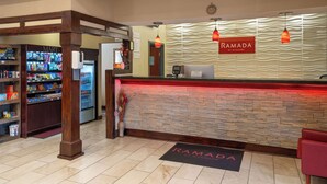 A reception area with a marble floor, a reception desk, a 'RAMADA' sign, a 'MART' section, and a vending machine. - Ramada by Wyndham Locust Grove (Locust Grove)