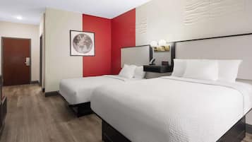 Une chambre d’hôtel avec deux lits, un mur d’accent rouge, une carte du monde encadrée, une table de chevet avec une lampe et une porte.