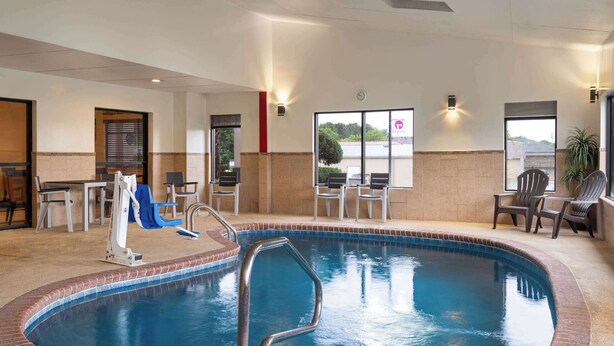 An indoor swimming pool with a blue tiled edge, a pool ladder, and a seating area with chairs and tables. - Ramada by Wyndham Locust Grove (Locust Grove)