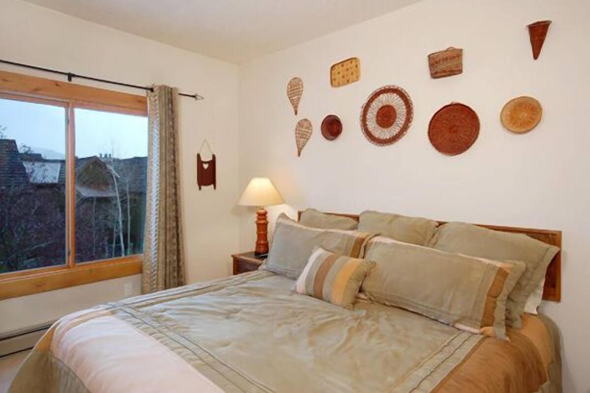 Une chambre à coucher avec un grand lit, une table de chevet avec une lampe et une fenêtre avec des rideaux.