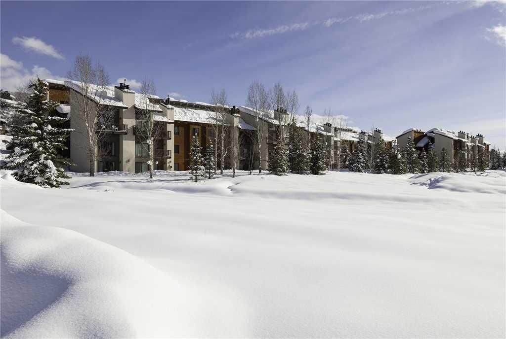 A row of modern buildings with snow-covered roofs and trees in a winter landscape.