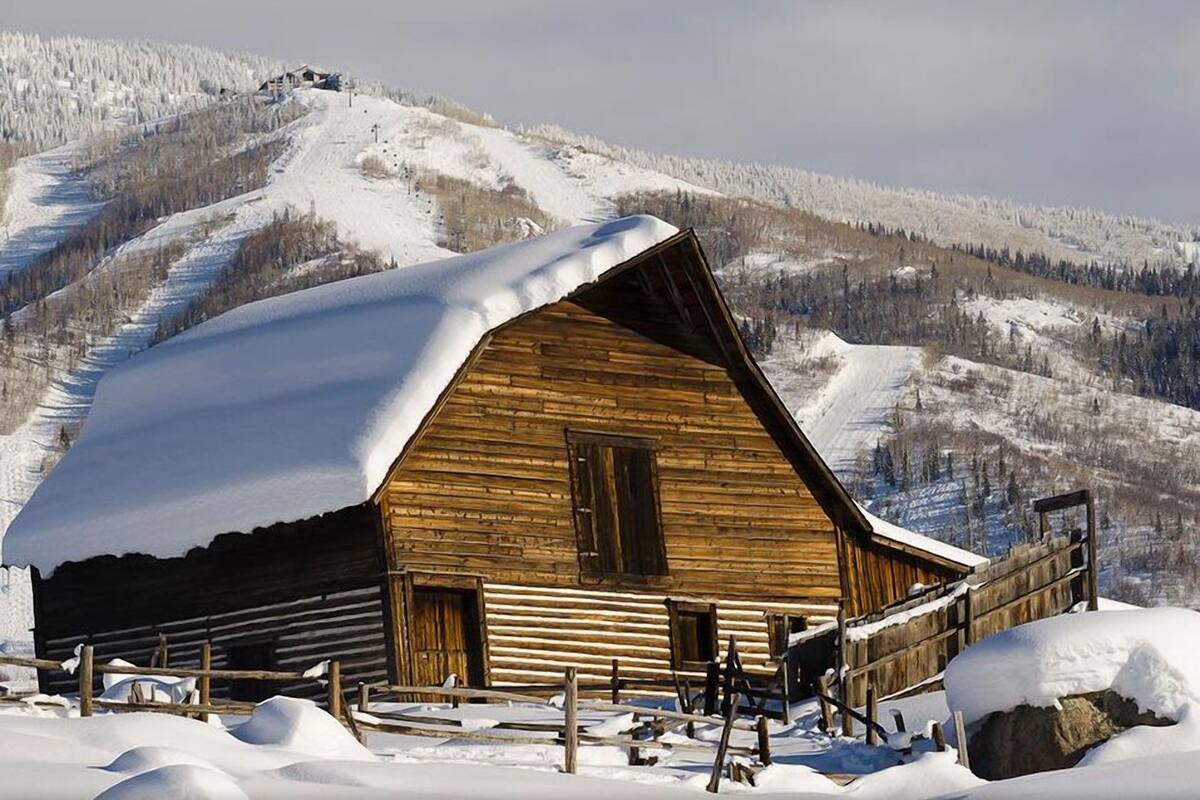 Une cabane en bois avec un toit en pente, entourée d’un paysage enneigé et avec une montagne boisée en arrière-plan.